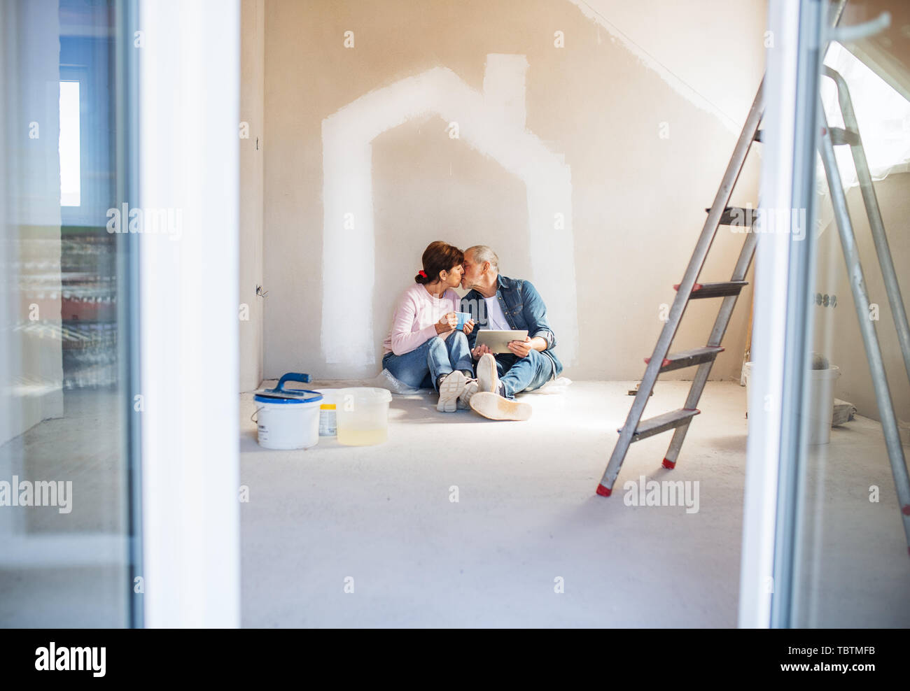 Senior couple painting walls in new home, kissing. Relocation concept. Stock Photo