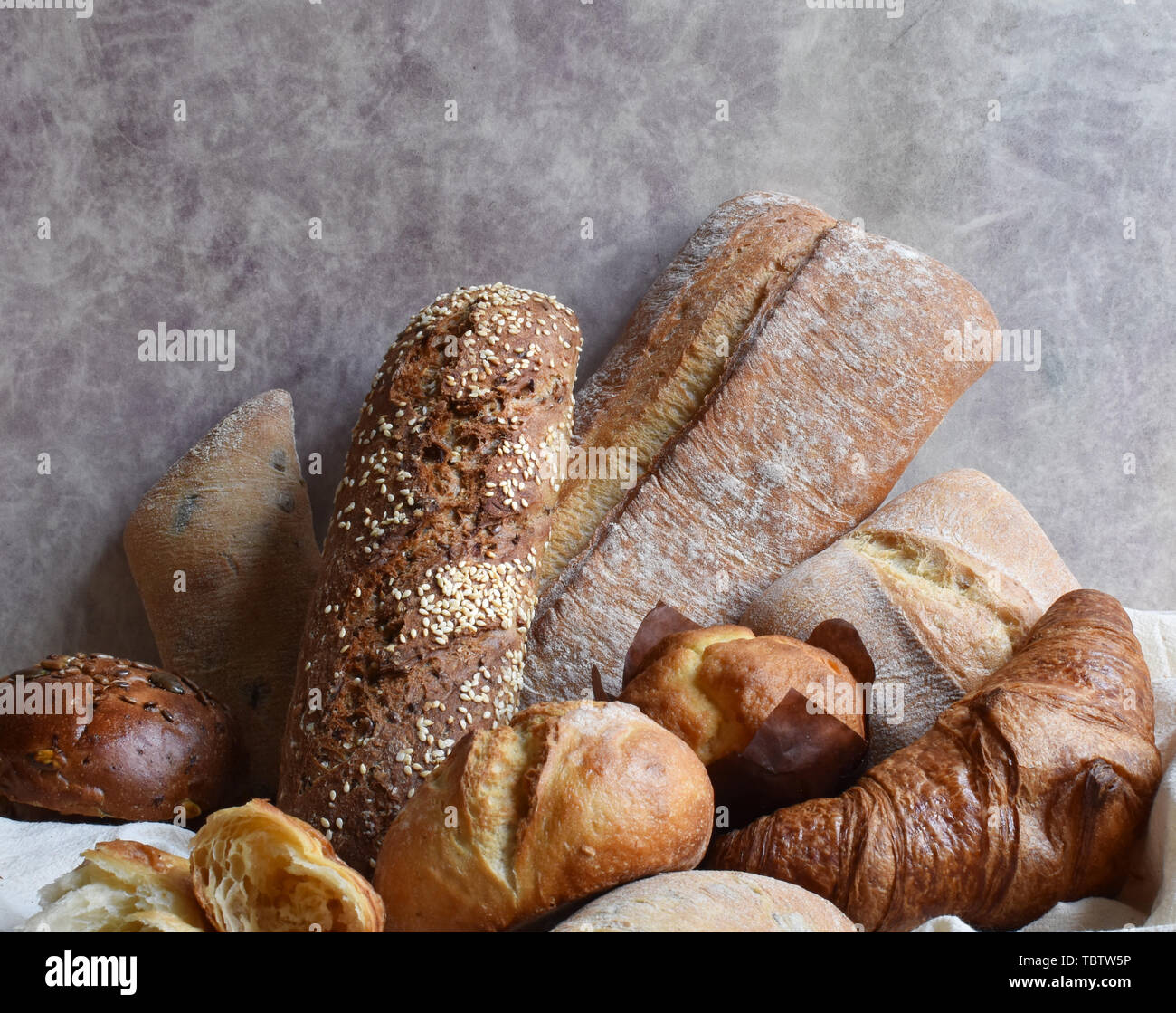 Different types of baking still life. Buns croissants, muffins and loaves, bread patties on textile drapery. Rustic style vintage bakery poster. Rural Stock Photo