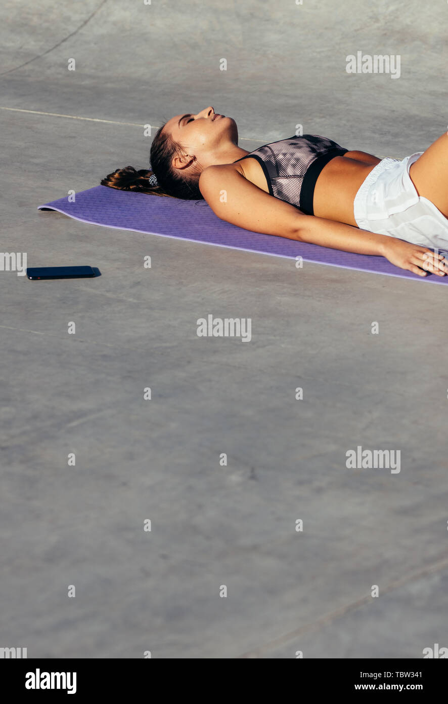 Young woman lying with her eyes closed on yoga mat. fitness female resting after training session. Stock Photo