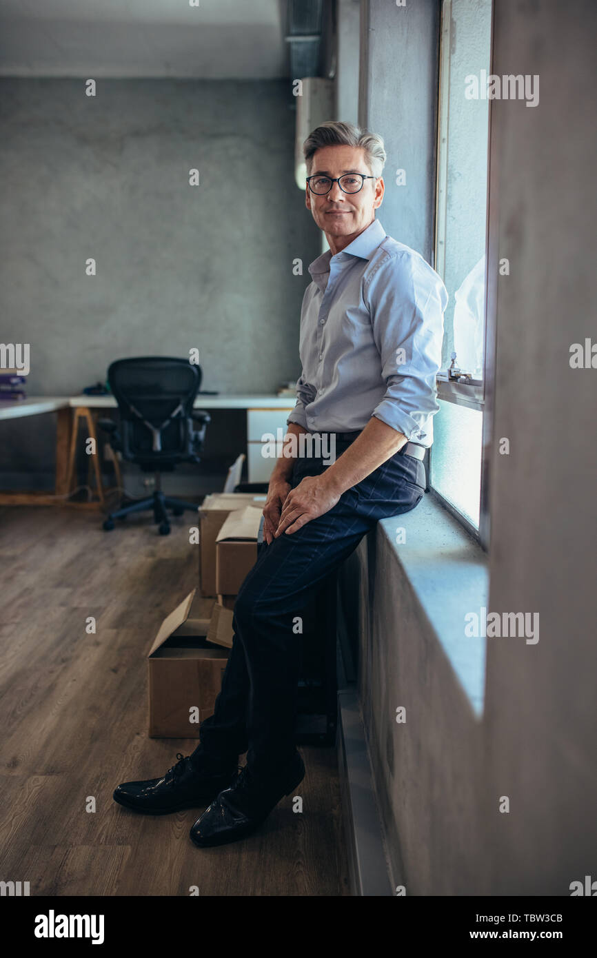 Man standing in office looking at camera. Dropshipping business owner leaning to a window sill at his office. Stock Photo