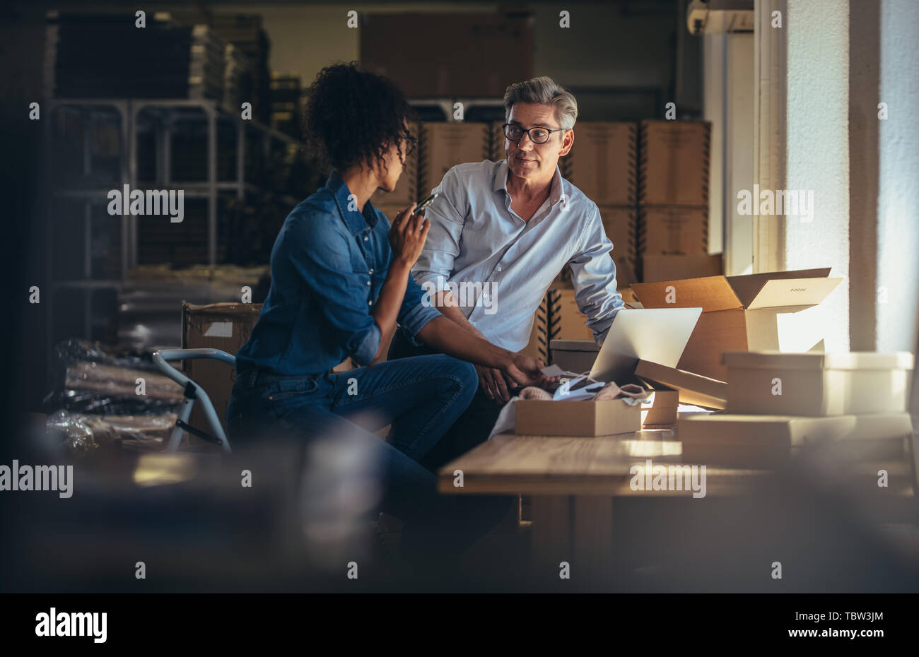 Two business partners working together at warehouse for online seller business. People discussing while preparing the package to delivery. Stock Photo