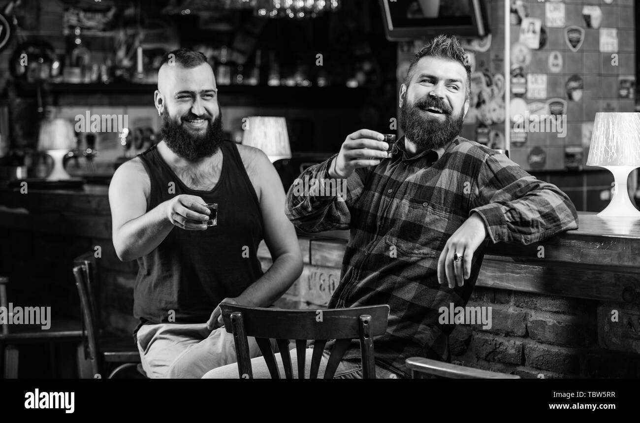 Men drunk relaxing at pub having fun. Strong alcohol drinks. Friends relaxing in pub. Friday relax in pub. Cheers concept. Hipster brutal bearded man drinking alcohol with friend at bar counter. Stock Photo