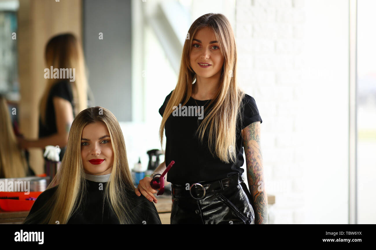 Young Blonde Hairstylist And Salon Female Client Smiling