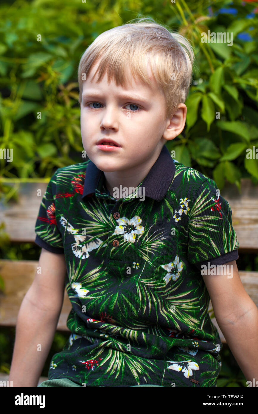 Blonde Little boy in green flowers shirt in the summer park Stock Photo