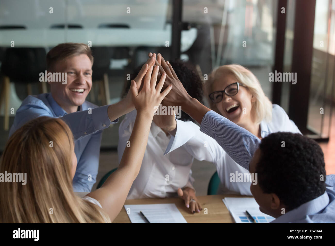 Diverse team of employees giving high five at briefing Stock Photo - Alamy
