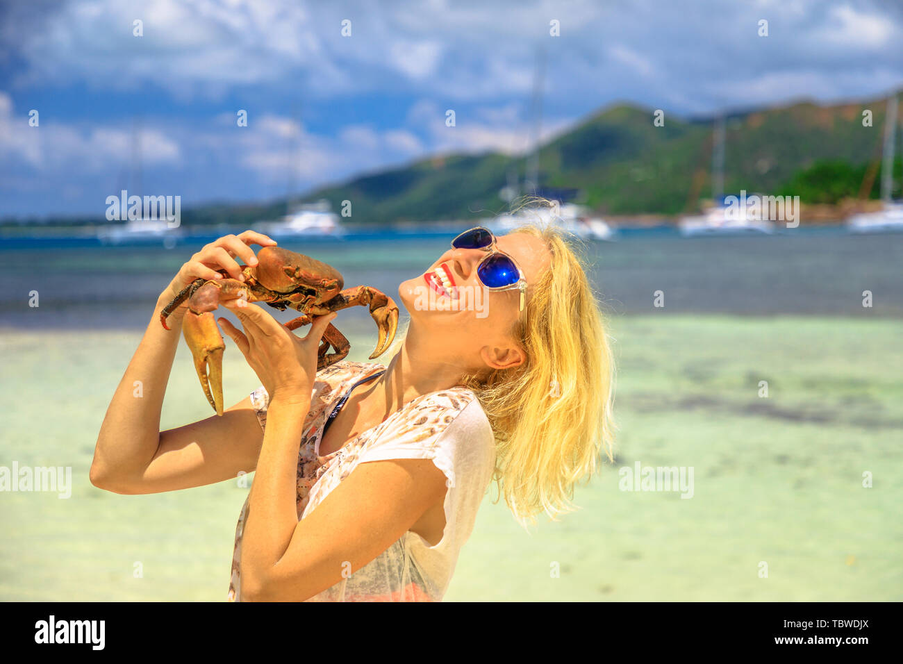 Tourism in Seychelles, Africa, Indian Ocean. Happy tourist woman holding an Ocypode Ceratophthalmus also called Ghost Crab with one claw being larger Stock Photo