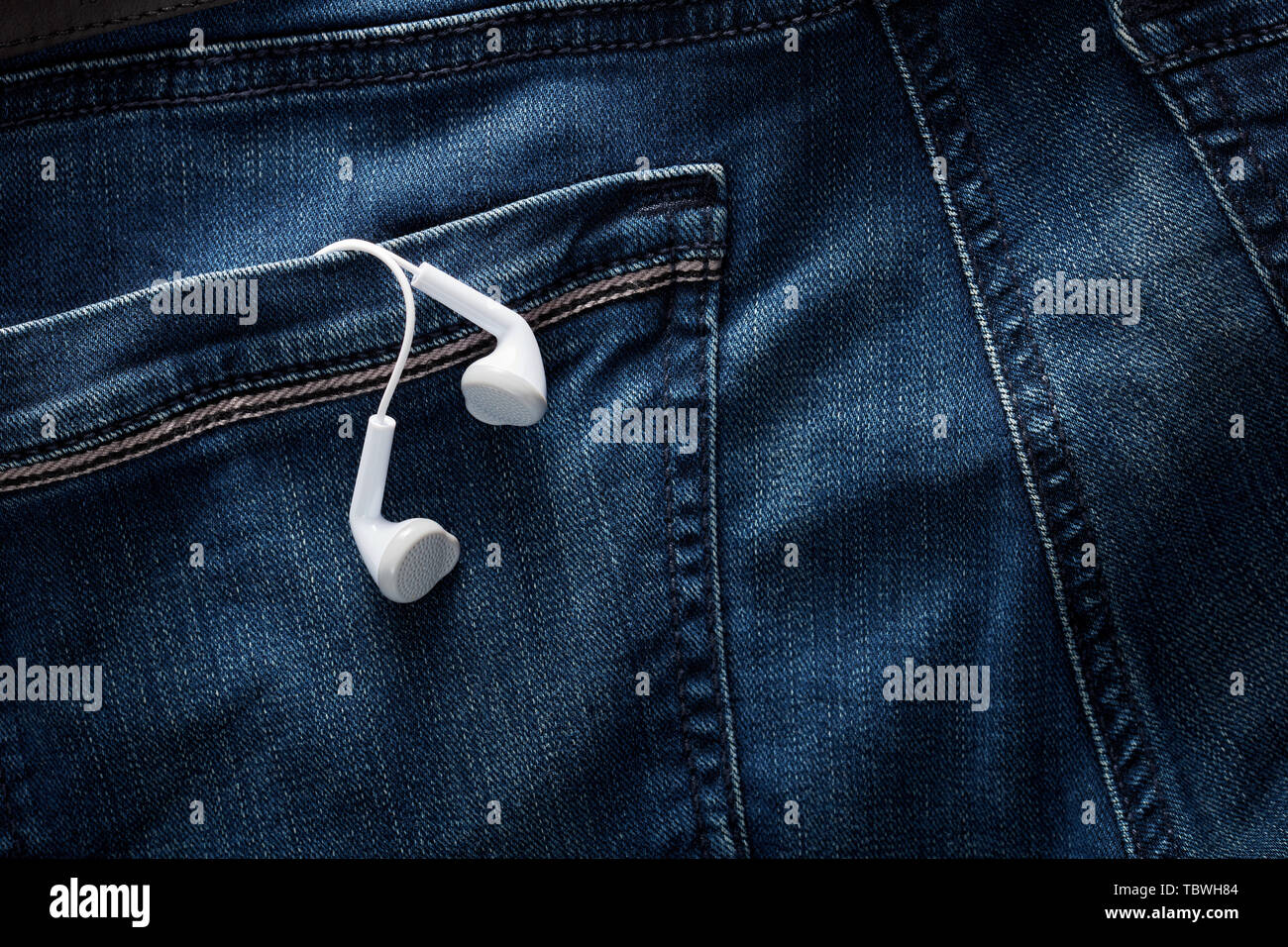 White earphones in the back pocket of a blue jean under dark dramatic moody lighting. Close up view. Stock Photo