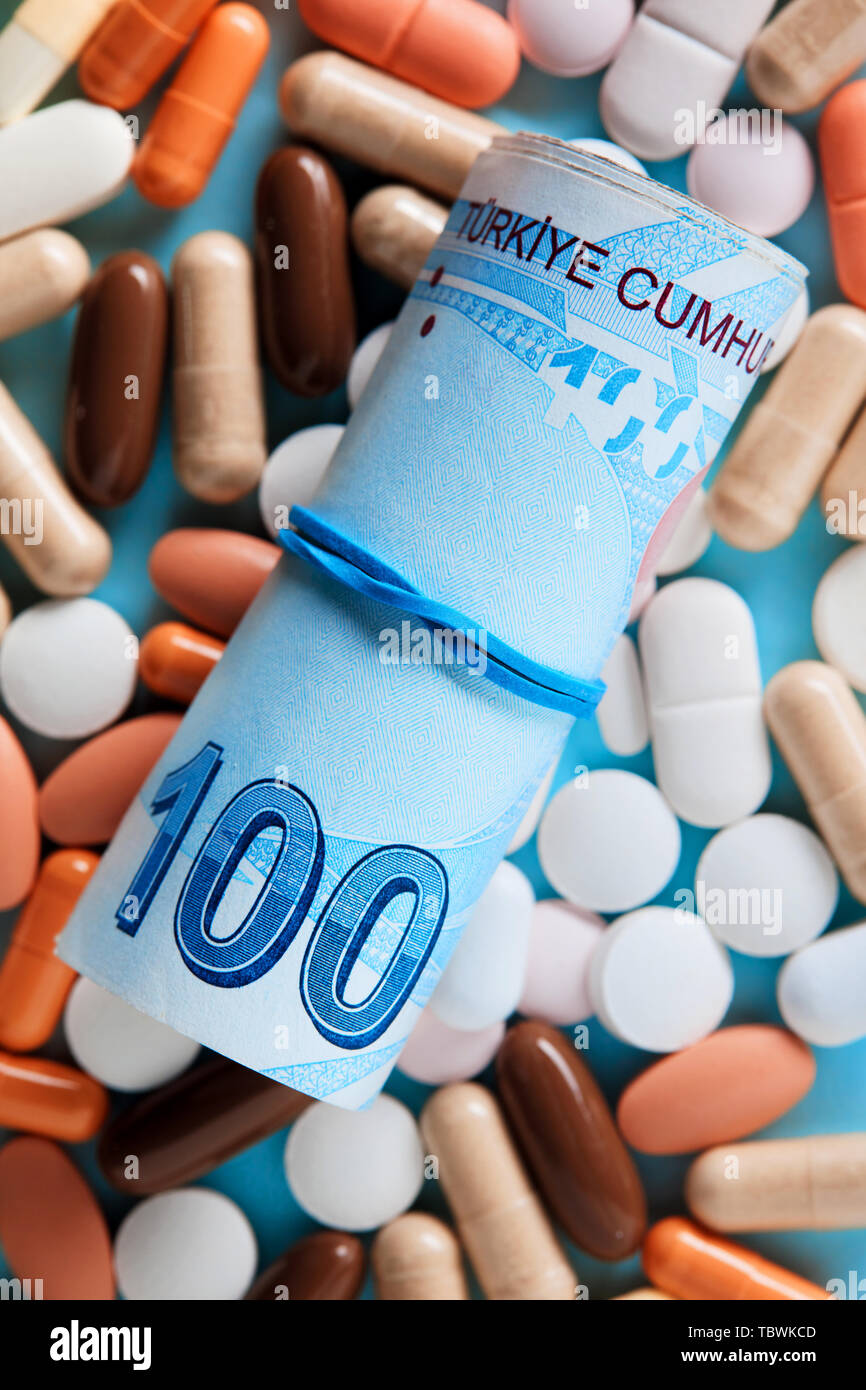 Rolled up bunch of one hundred Turkish Lira bills over the medical pills. Expensive medicine and healthcare industry concept. Overhead macro view. Stock Photo