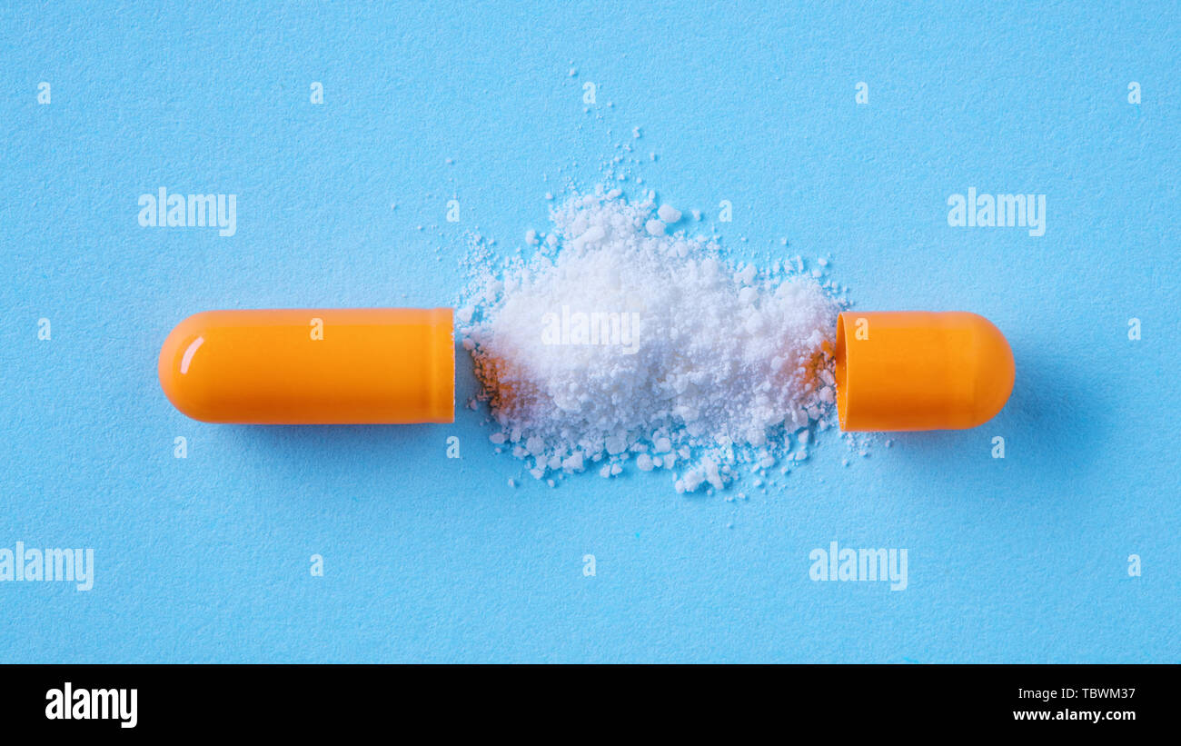 Close up split open medical pill capsule with spilled white powder on