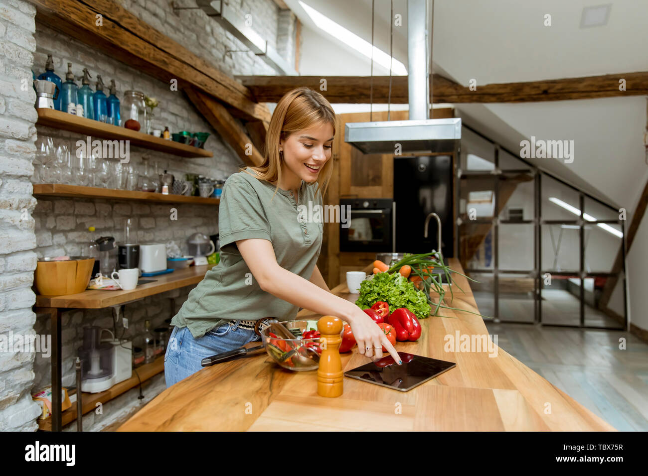 Young woman preparing food in the rustic kitchen while using digital tablet Stock Photo