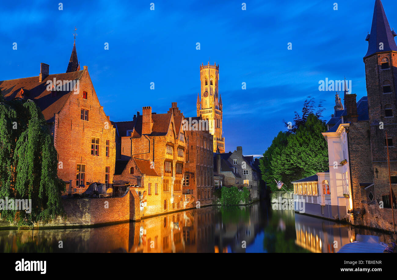Famous view of Bruges tourist landmark attraction - Rozenhoedkaai canal with Belfry and old houses along canal with tree in the night. Belgium Stock Photo