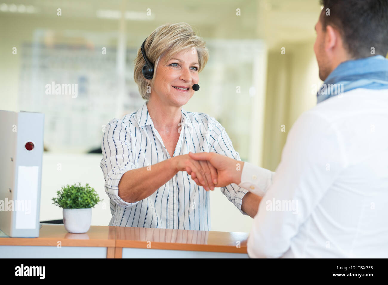 mature receptionist wearing headset greeting man with a handshake Stock