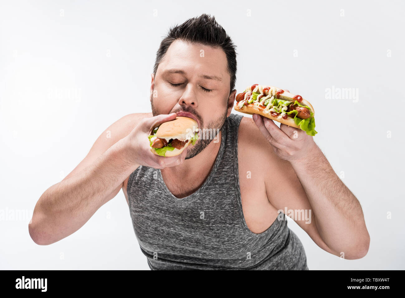 overweight-man-in-tank-top-eating-tasty-hot-dog-isolated-on-white-stock