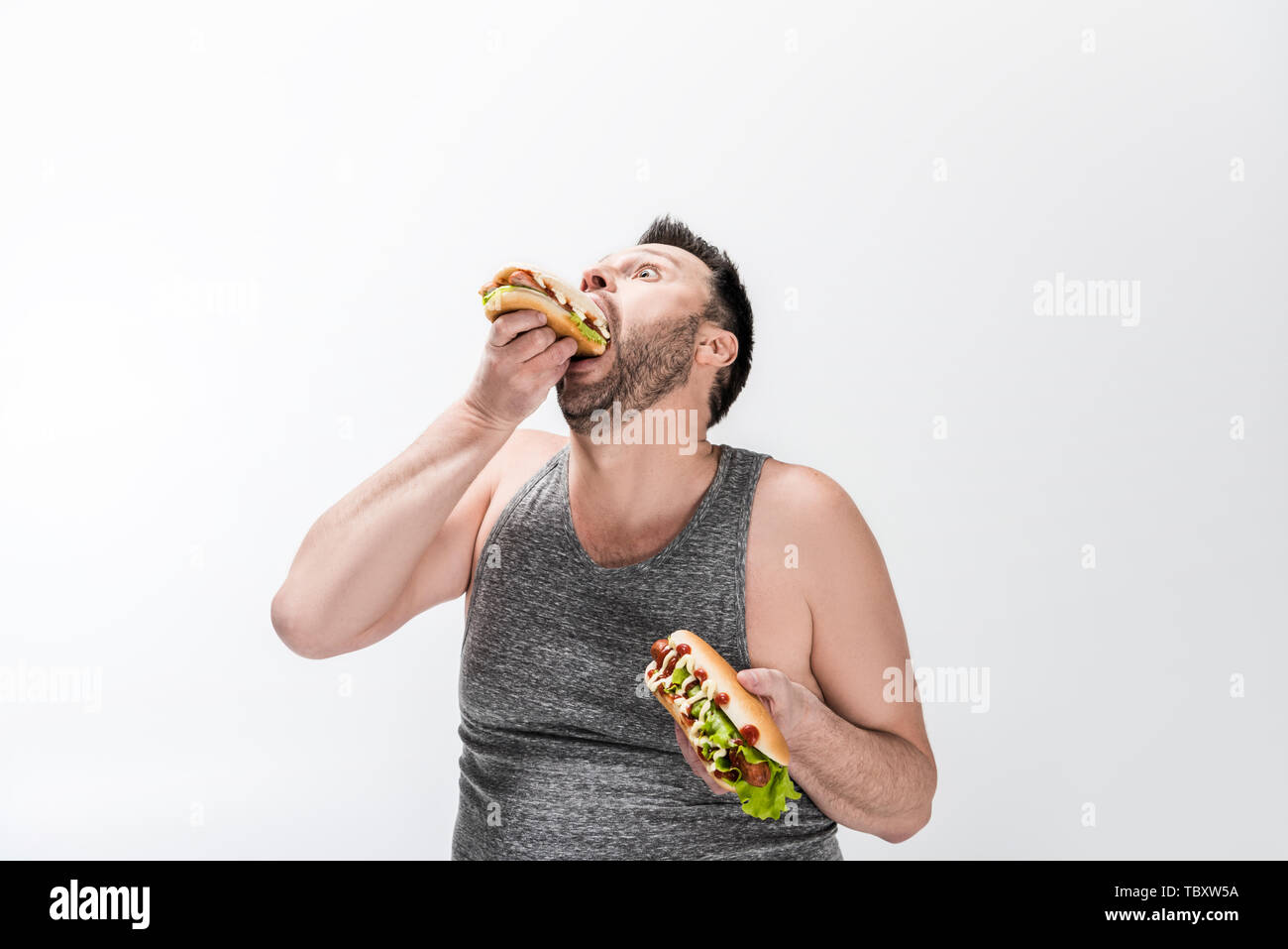hungry overweight man in tank top eating hot dog on white Stock Photo