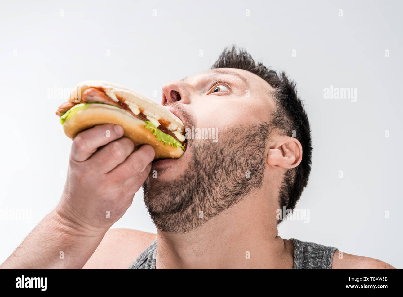 close up view of overweight man in tank top eating hot dog isolated on white Stock Photo
