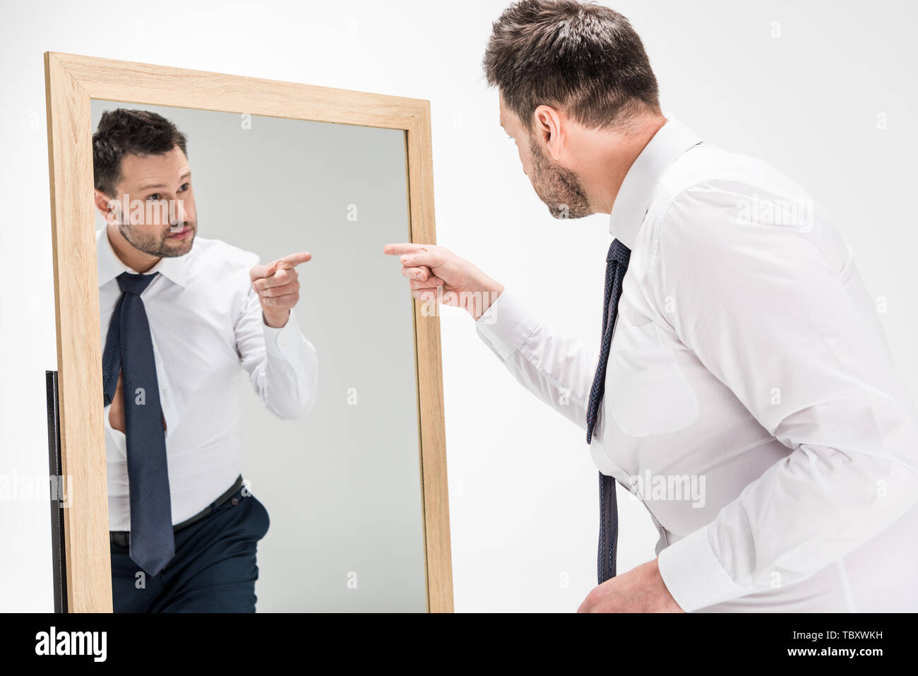 overweight man in formal wear pointing with finger at reflection in mirror on white Stock Photo