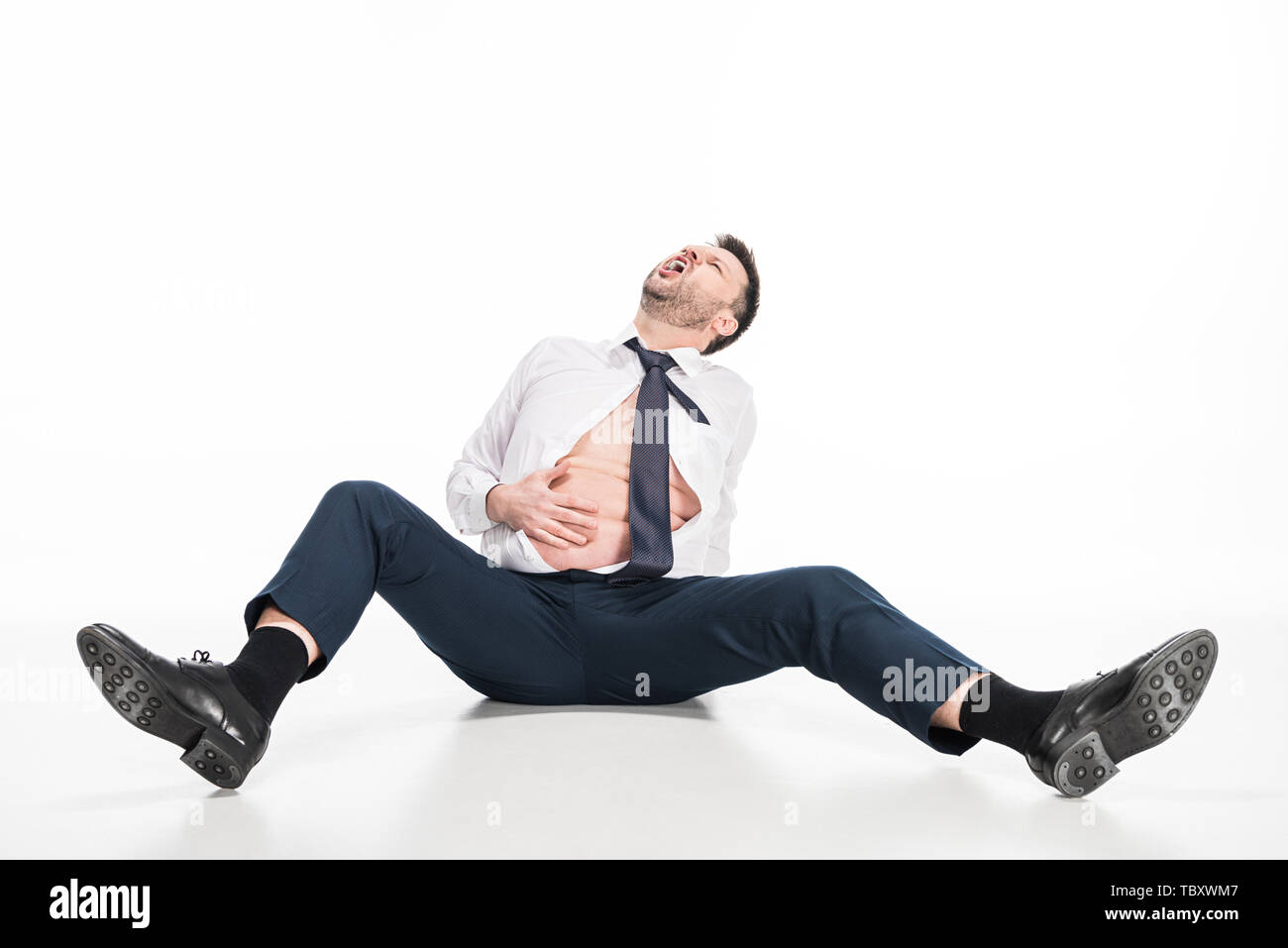 angry overweight man in tight formal wear touching belly while sitting on white Stock Photo