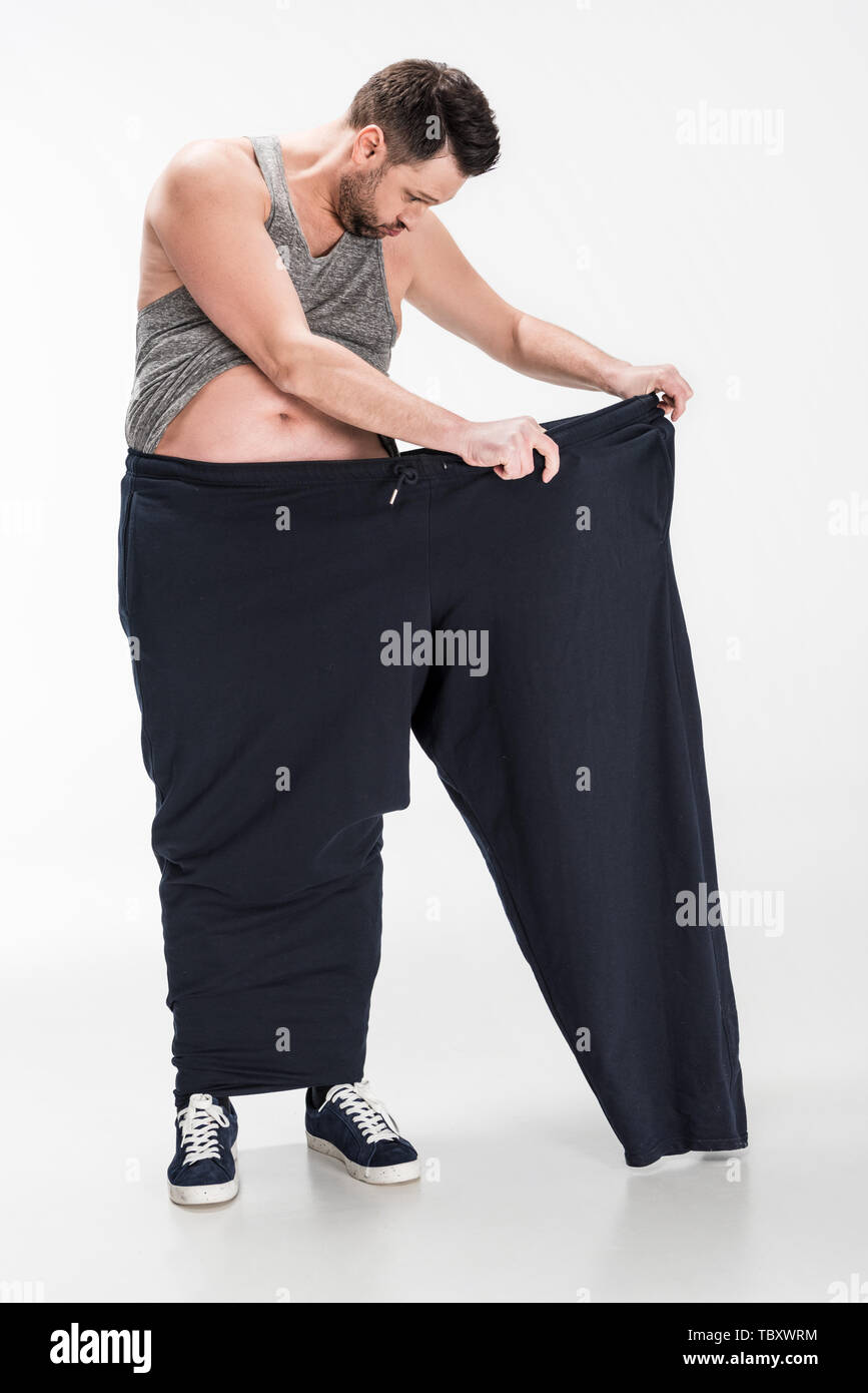 overweight man in tank top holding oversize pants after weight loss on ...