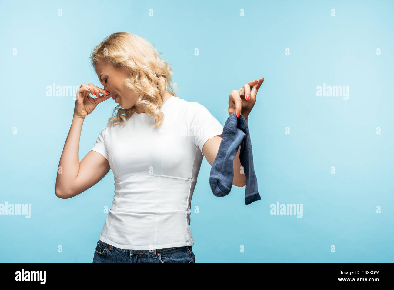 curly blonde woman touching nose while holding smelly dirty sock on