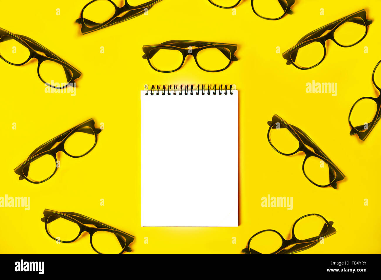 Notepad with trendy glasses on light yellow background. Stock Photo