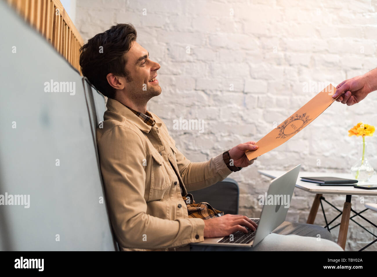 Smiling freelancer with laptop holding menu in cafe Stock Photo