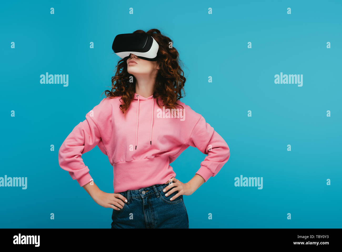 curly girl wearing virtual reality headset while standing with hands on ...