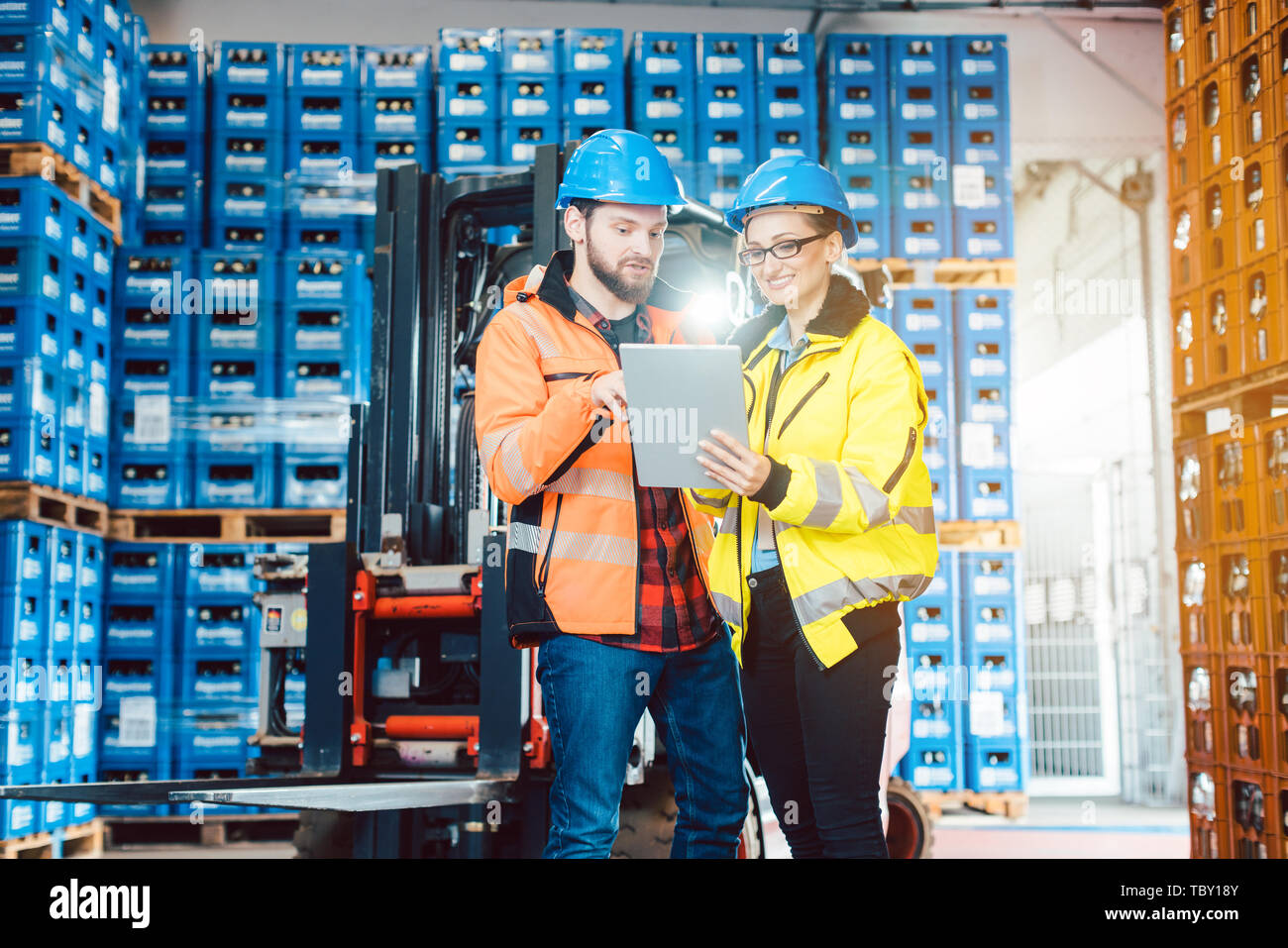 Workers in warehouse checking data on tablet computer with forklift in the background Stock Photo