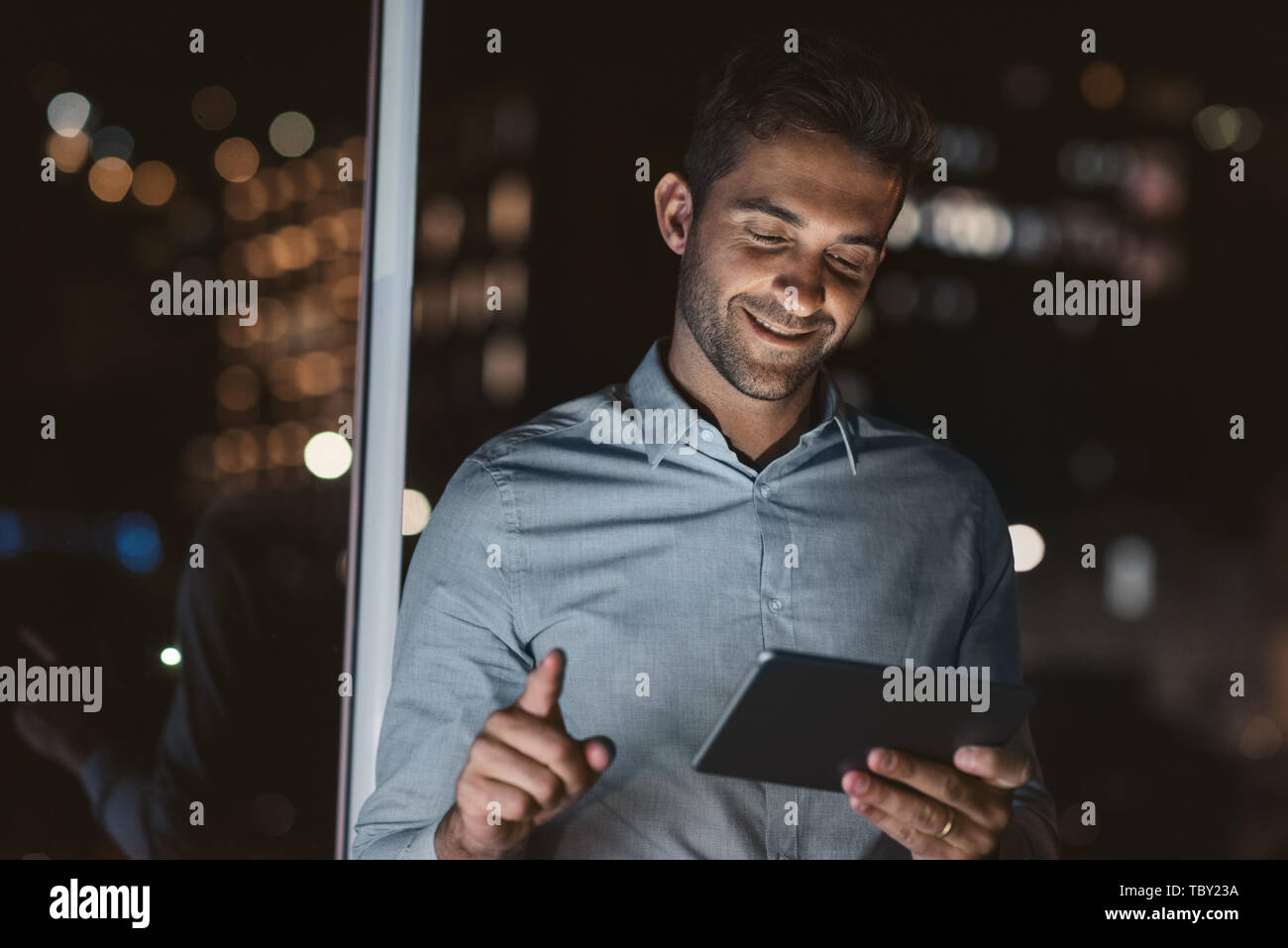 Smiling businessman standing in his dark office using a tablet Stock ...