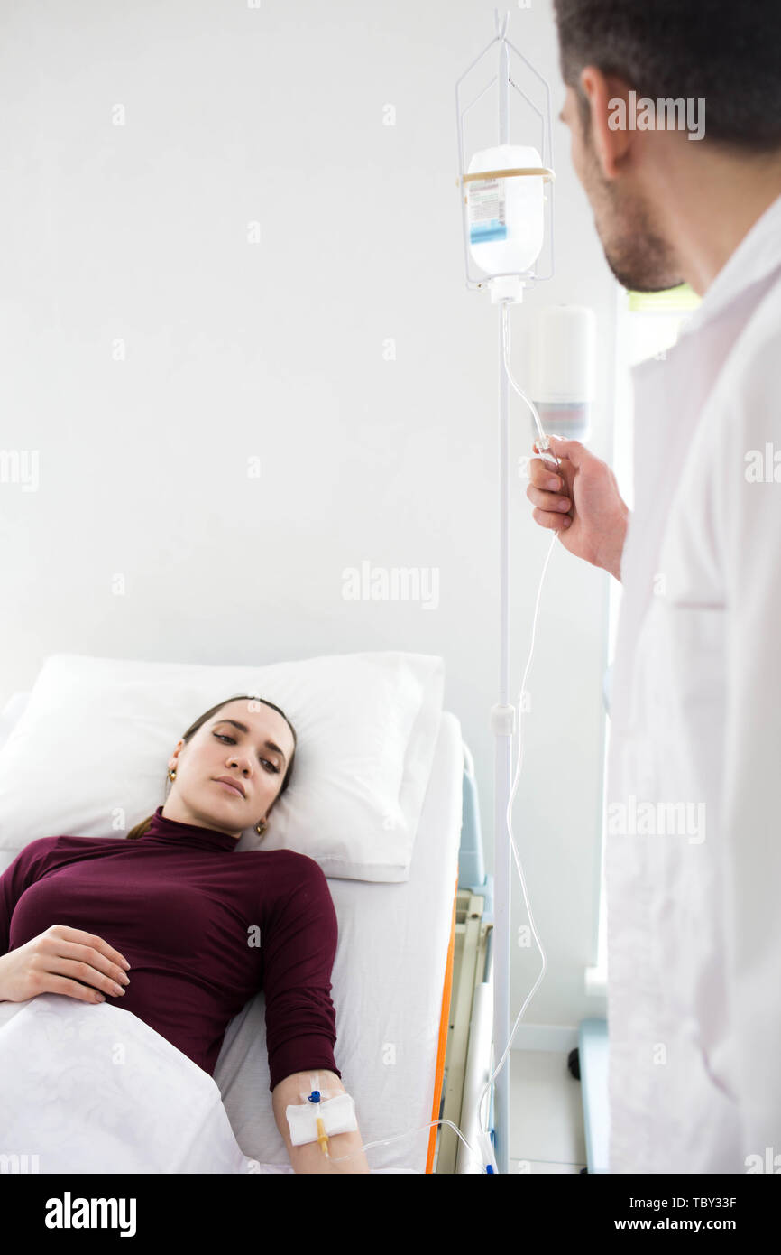 Woman lying in hospital bed, patien trecovery , treatment IV Drip. doctor assistance young woman Stock Photo
