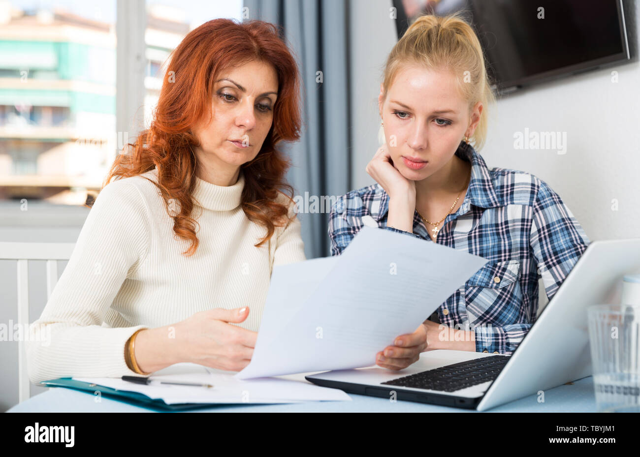 Portrait of sad mature woman and daughter signing documents at table ...