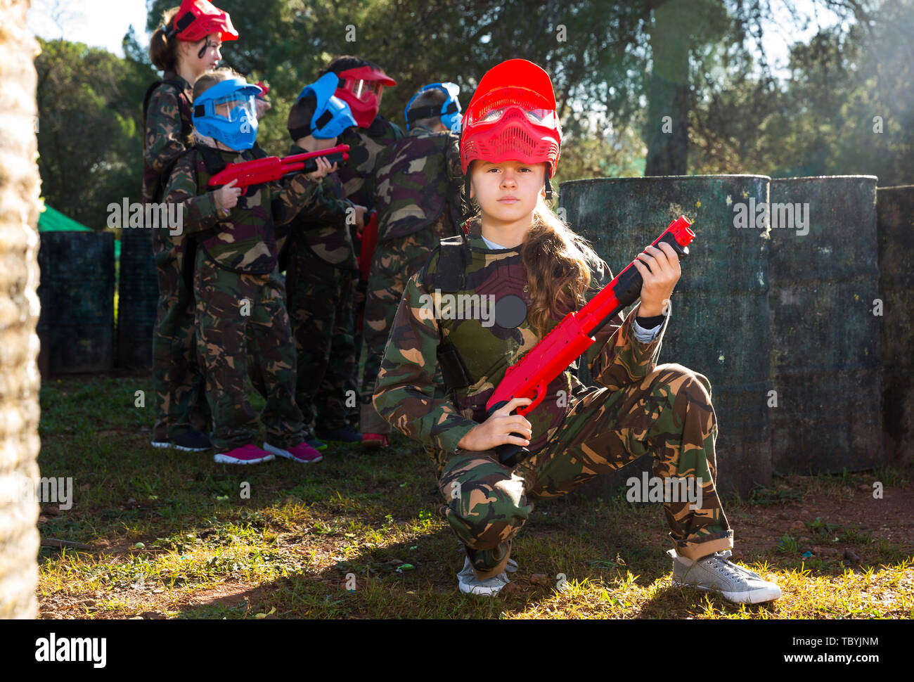 sportive girl paintball player in camouflage standing with gun before playing outdoors Stock Photo