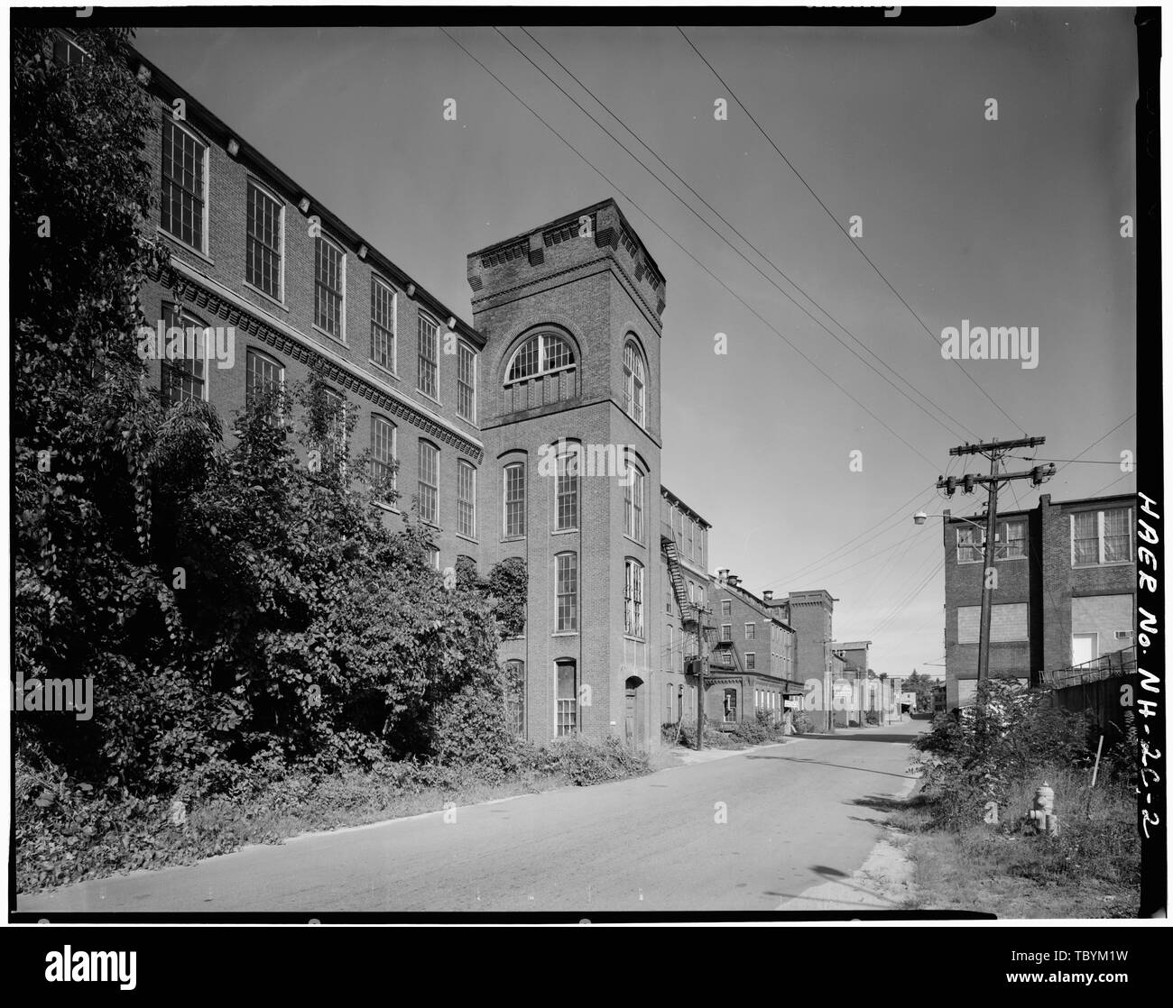 Monadnock Mill No. 3 from the southwest. A photo dating from ca. 1900 (collection of the Claremont Historical Society) shows that the thermal windows on the top level of the tower were originally unglazed, and that there were 'areaways' which have been filled in. These areaways originally allowed light to enter the basement level through eight over eight sash windows.  Monadnock Mills, Mill No. 3, Claremont, Sullivan County, NH Stock Photo