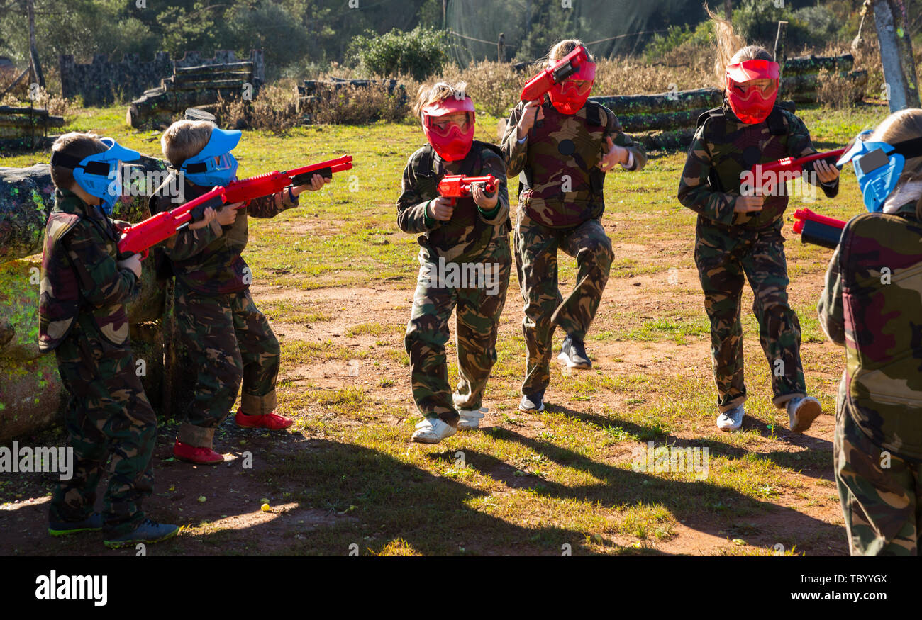 Teams of sportive kids facing on battlefield in outdoor paintball arena