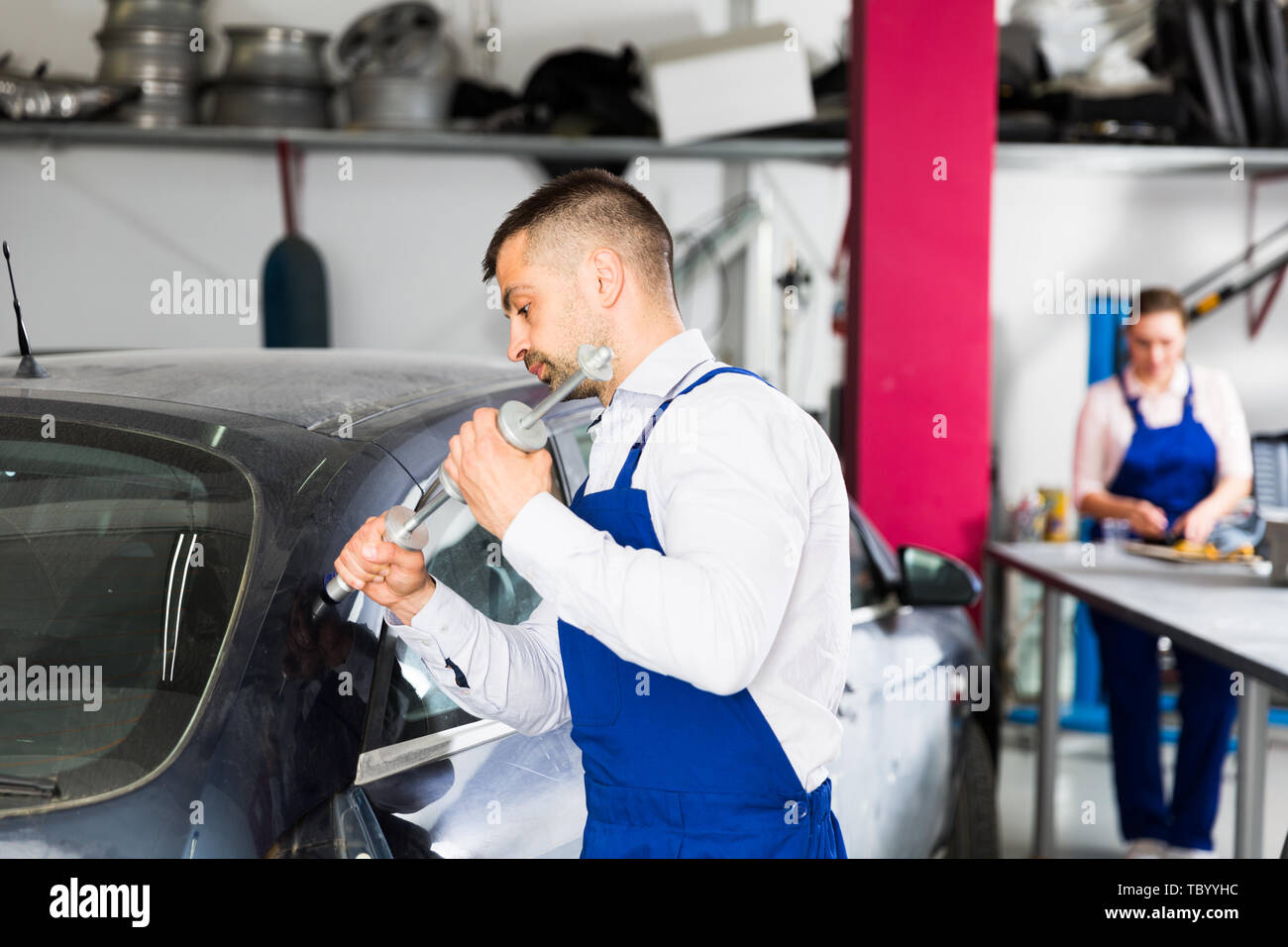 Concentrated mechanic performing car body repair at auto workshop with tools for repairing dents Stock Photo