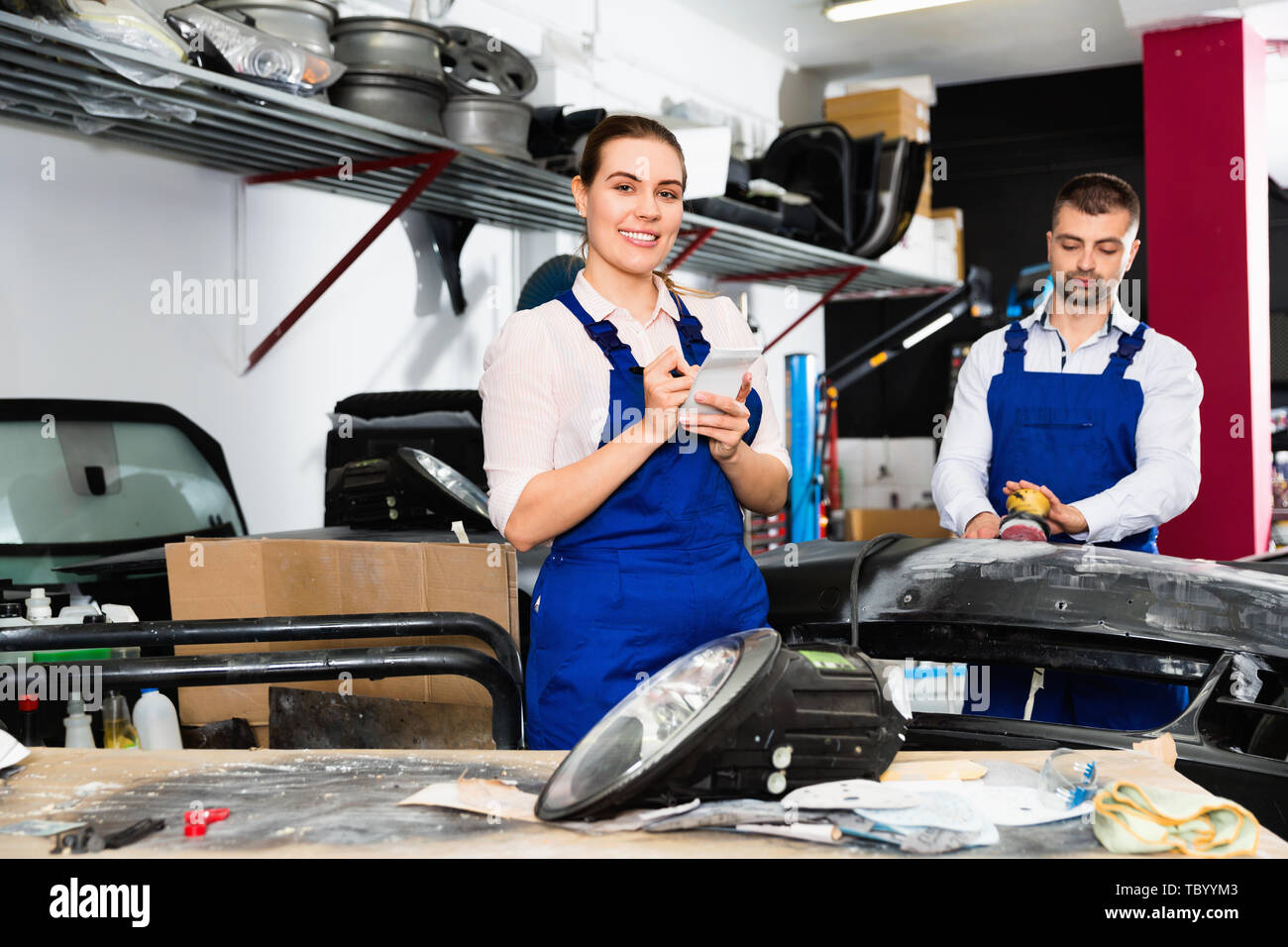 Professional cheerful positive smiling female mechanic recording list of works on car repair in auto repair shop Stock Photo