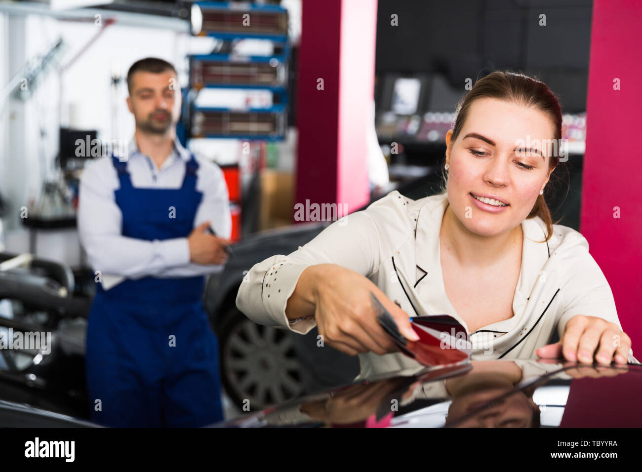 Smiling female client with paint samples choosing color for painting car at auto repair shop Stock Photo