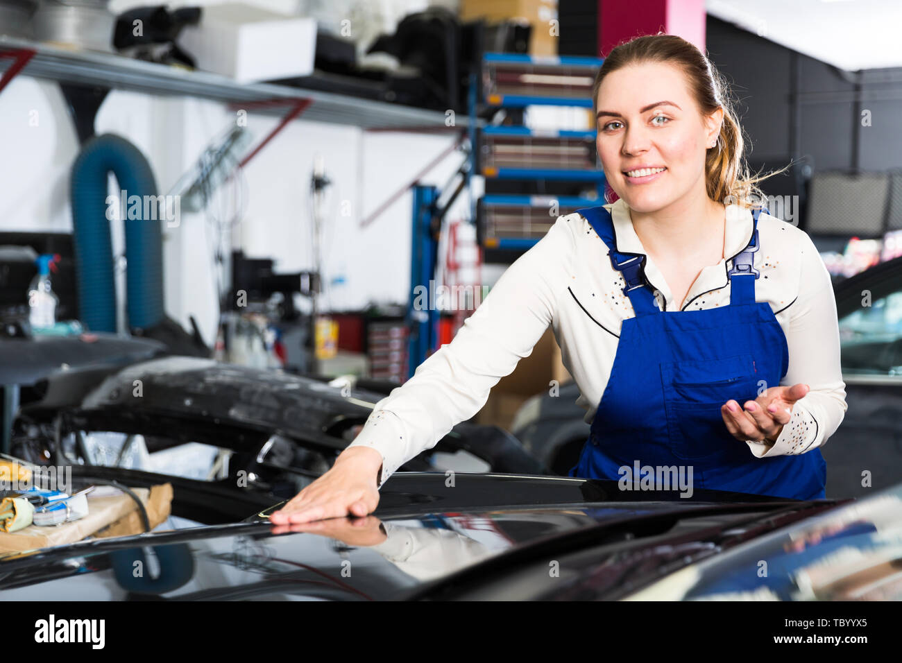 Smiling girl auto mechanic showing car after repainting at auto service Stock Photo