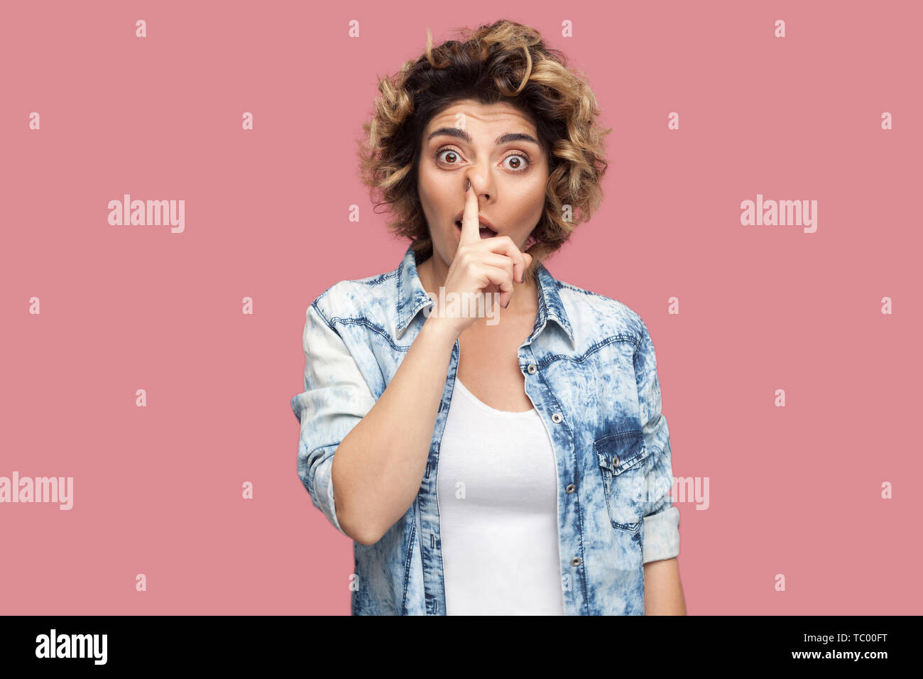 Portrait of crazy foolish young woman with curly hairstyle in casual blue shirt standing with finger on her nose, drilling and looking at camera. indo Stock Photo