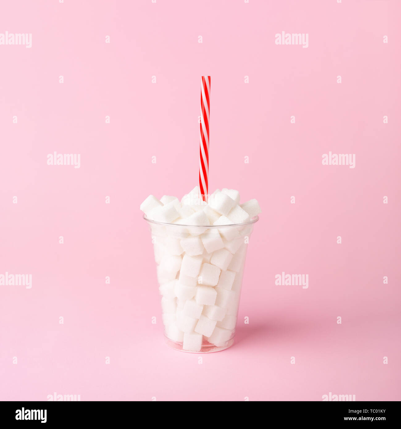 Plastic cup with straw full of sugar cubes on pastel pink background. Unhealthy food concept. Minimal, vertical, side view. Stock Photo