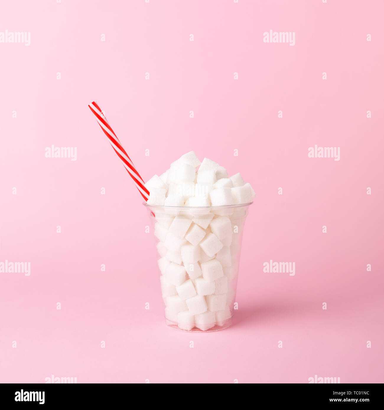 Plastic shake glass with straw full of sugar cubes on pastel pink background. Unhealthy drink concept. Minimal, vertical, side view. Stock Photo