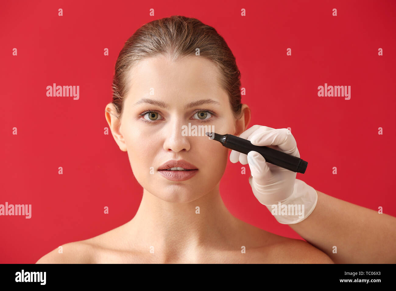 Plastic surgeon applying marking on female face against color