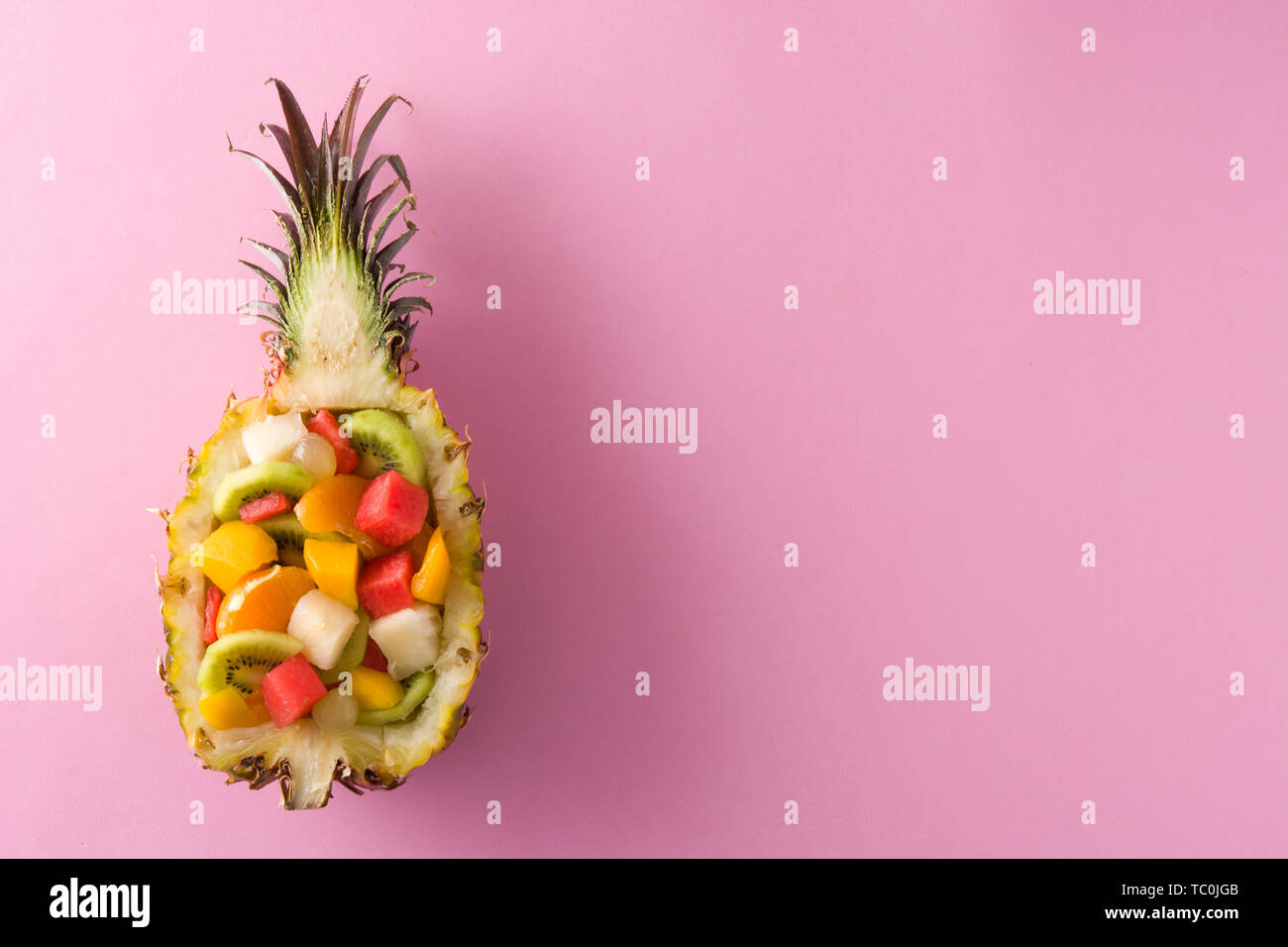 Mix fruit served inside pineapple on pink background Stock Photo