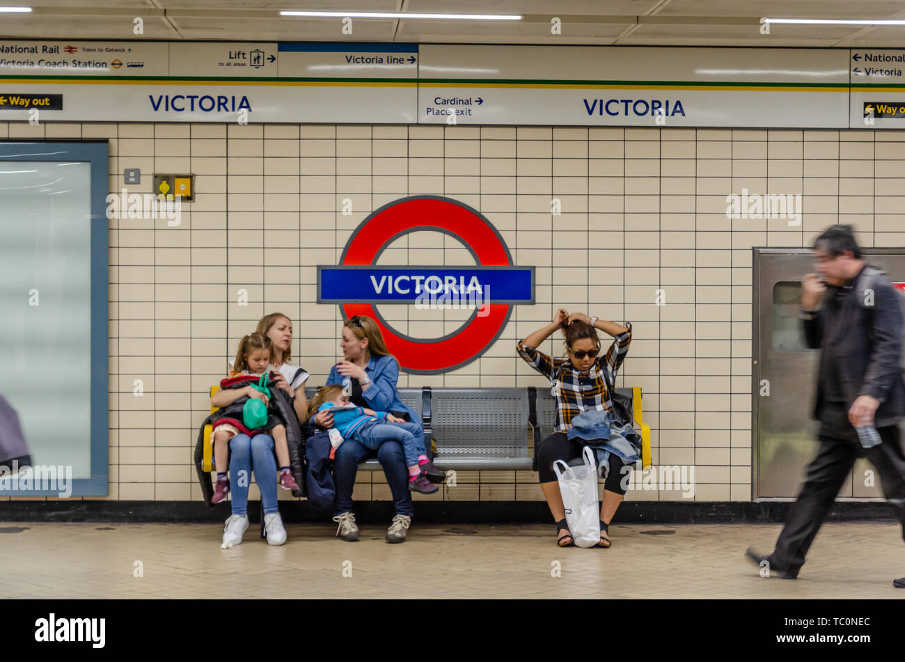 People sit on a bench on the platform at Victoria London Underground tube station. Stock Photo