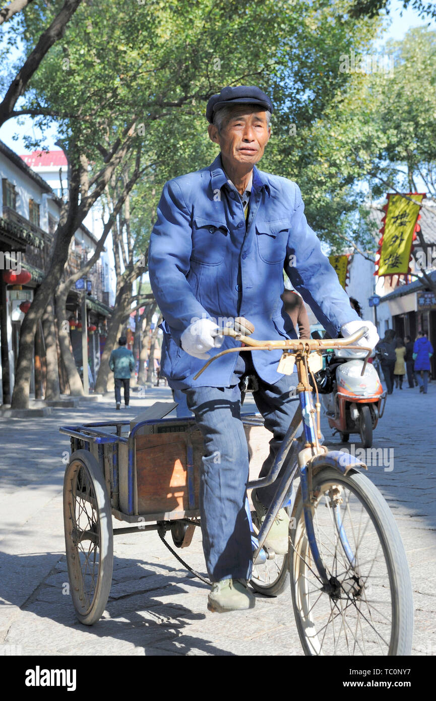 Tongli, China-November 28, 2008: Old man riding a tricycle in the shopping area of the town Stock Photo