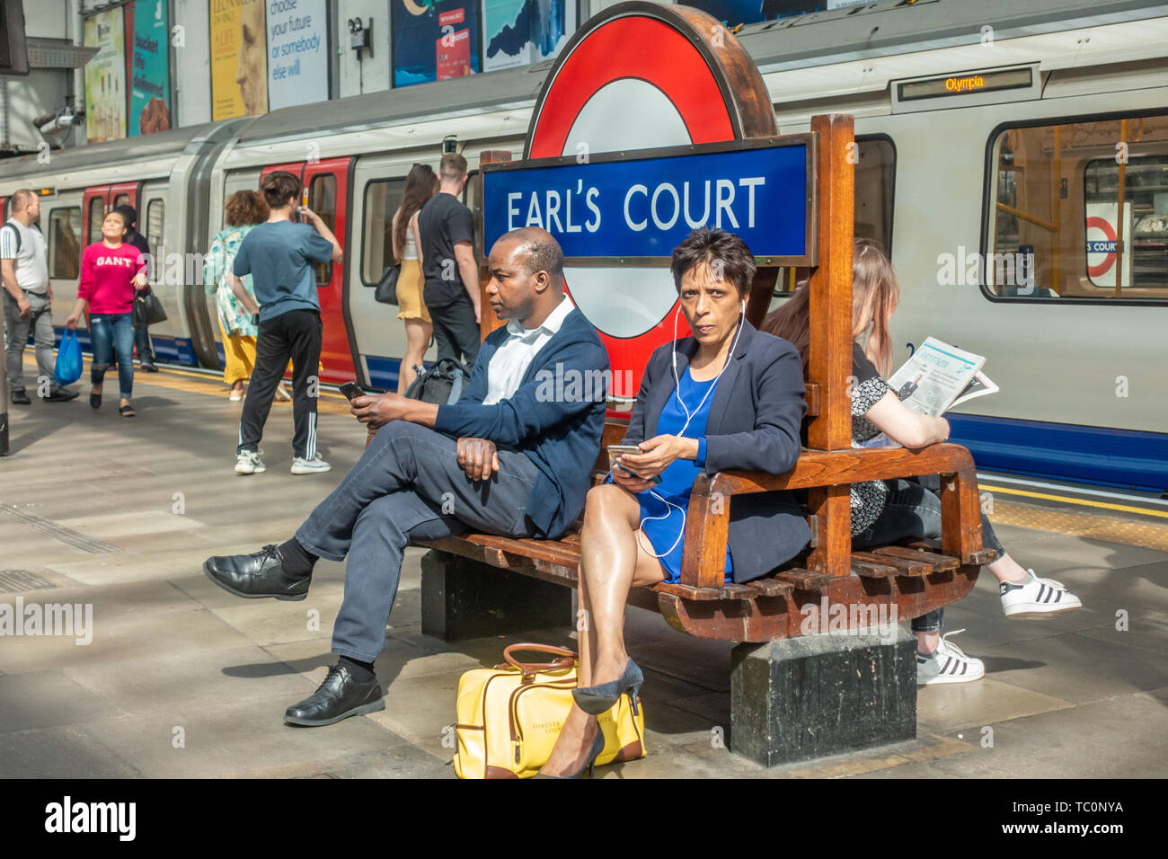 People sit on a bench on the platform at Earl's Court London Underground Station Stock Photo