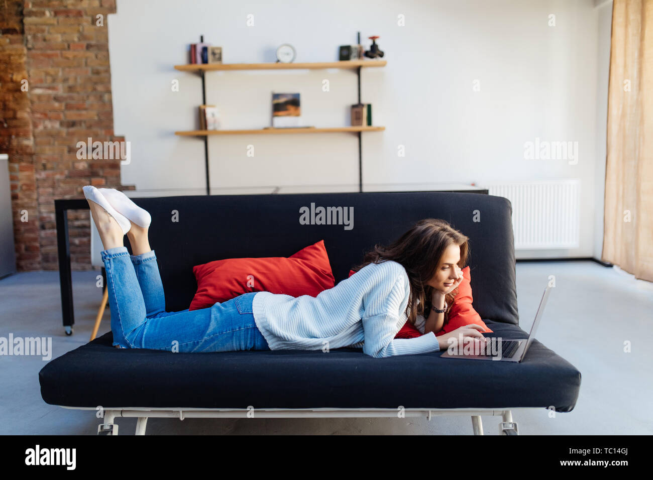 Woman lying on a sofa using a laptop in her living room Stock Photo - Alamy