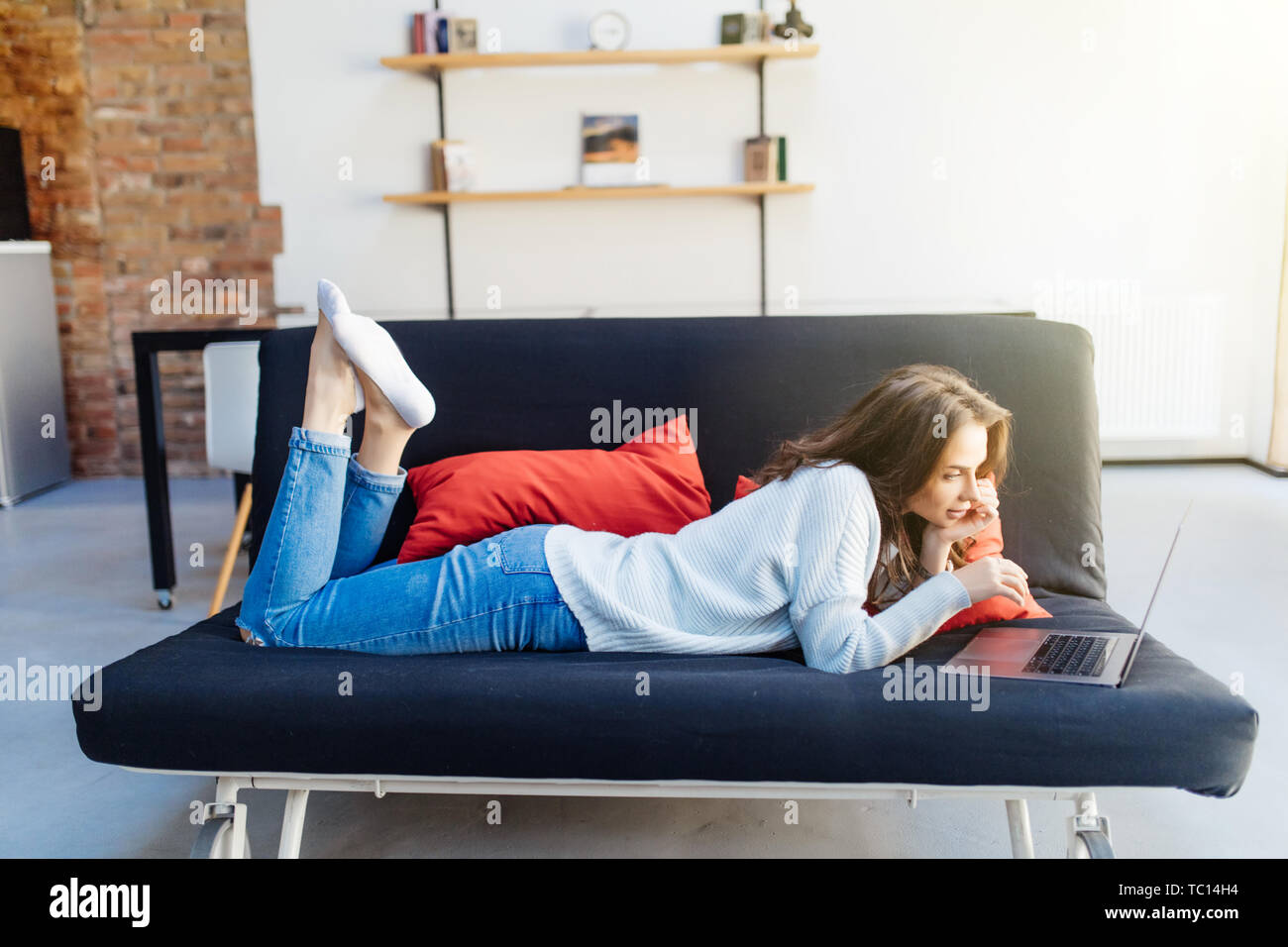 Young woman lying on couch with laptop Stock Photo - Alamy
