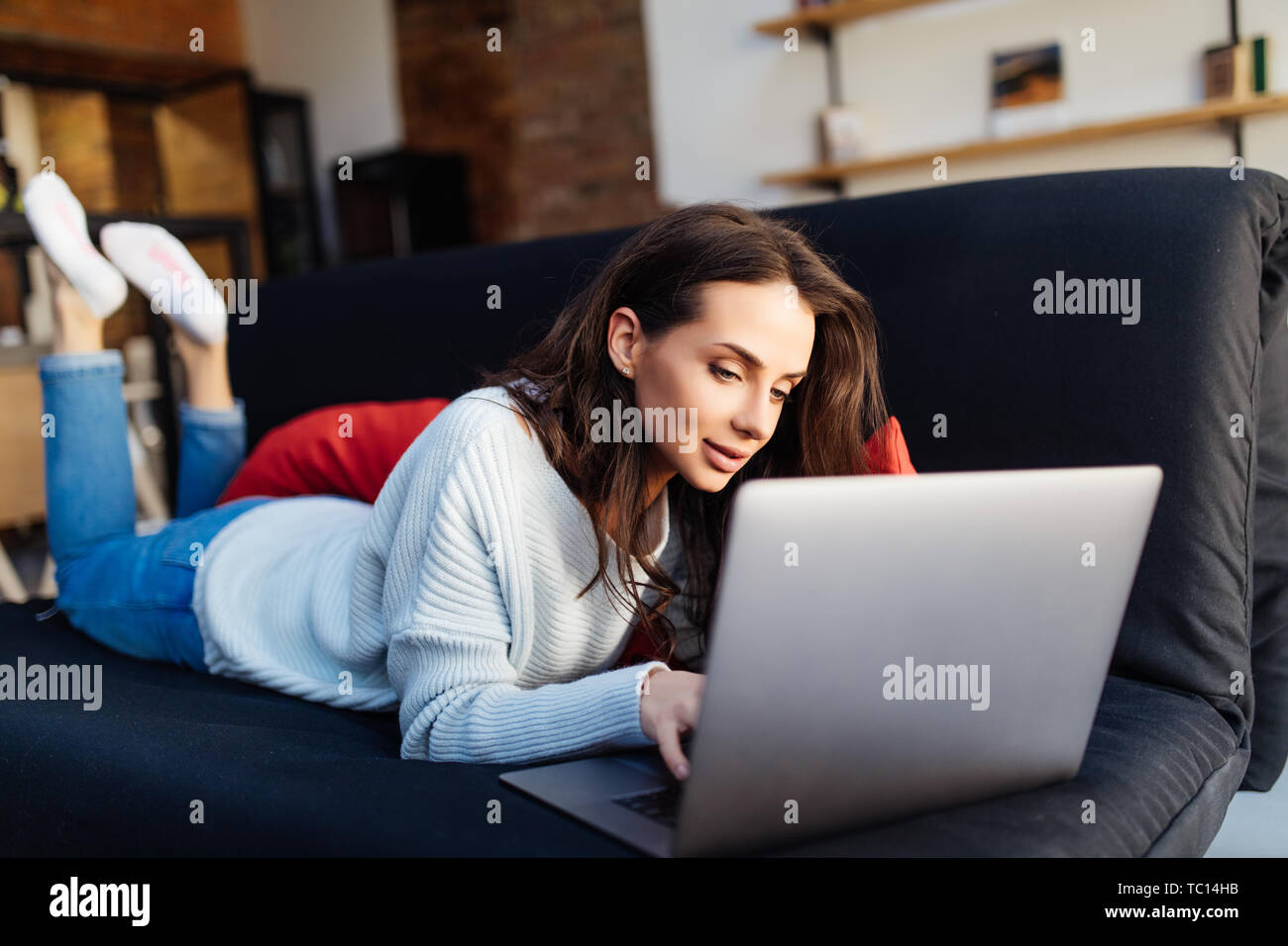 Young woman lying on couch with laptop Stock Photo - Alamy