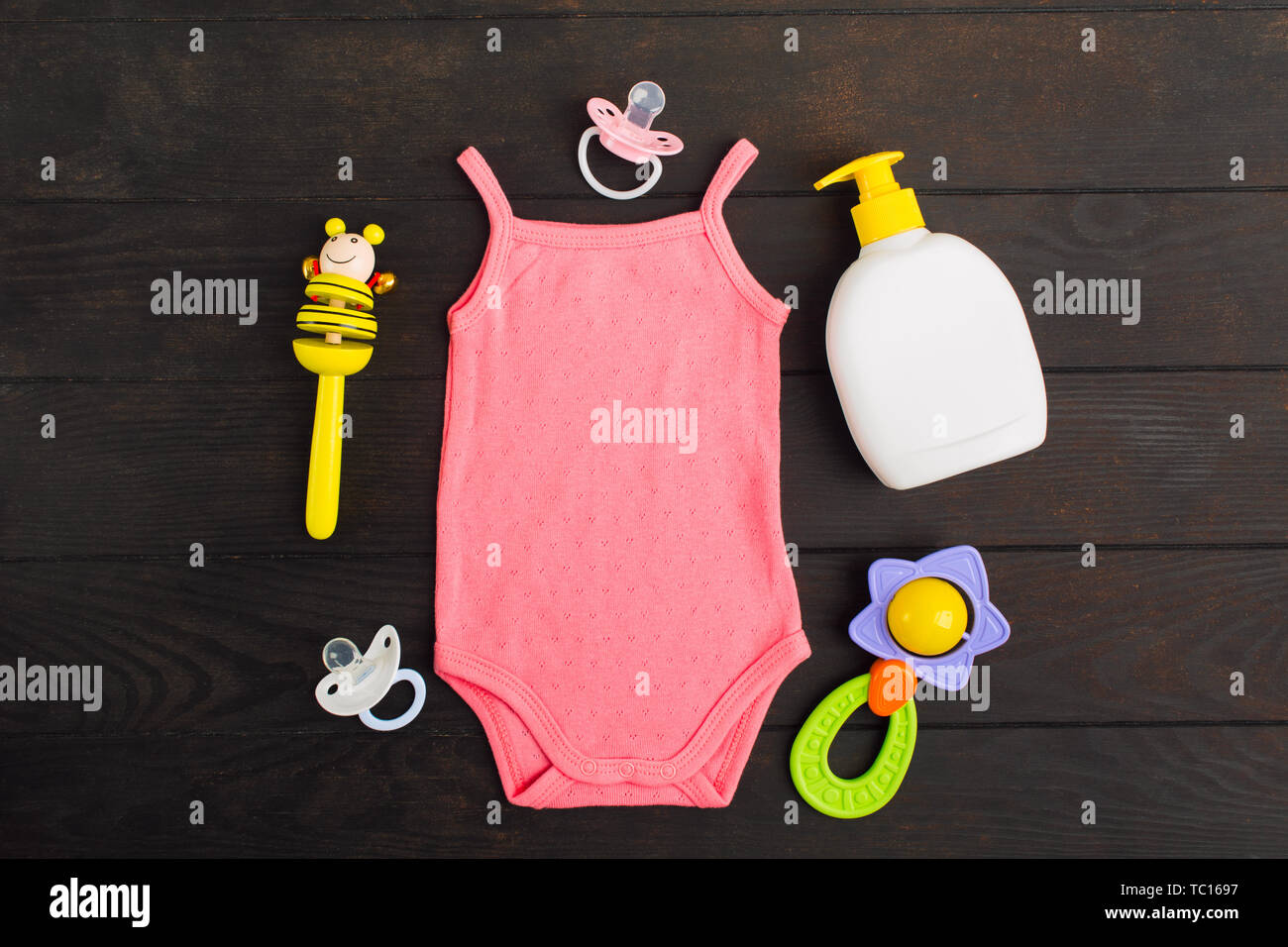 Baby accessories - pink bodysuit, soap, pacifier and rattle over wooden background. Flat lay Stock Photo