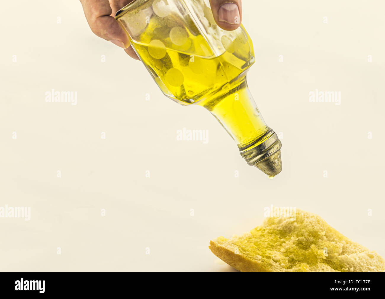 Close-up of olive oil pouring on slice of bread on white background, healthy food Stock Photo